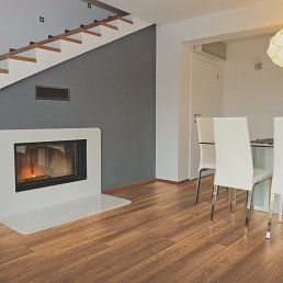 A modern living room with wooden floor, fireplace, and white chairs.