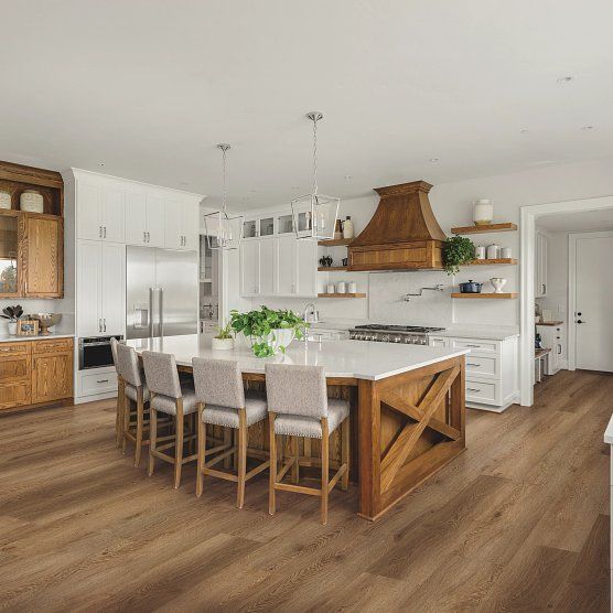 Spacious kitchen with wood flooring, large island with seating, and wood and white cabinetry.