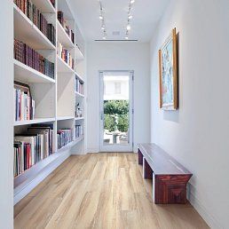 A hallway with a bookshelf, wooden bench, and door to a garden. Light wood floors and white walls.