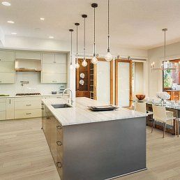 Modern kitchen with island and pendant lights, neutral tones, light wood flooring, and a dining area.