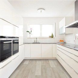 Modern white kitchen with light wood-look flooring, white cabinetry, and stainless steel appliances.