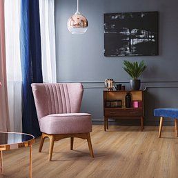 Pink armchair in a room with wood flooring, gray walls, and a hanging copper light.