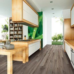 Modern kitchen with wood cabinets and flooring, green accent wall, and natural light.