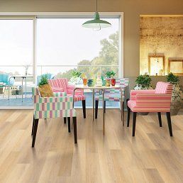 Dining room with a round table, colorful chairs, and wood flooring, overlooking a balcony.