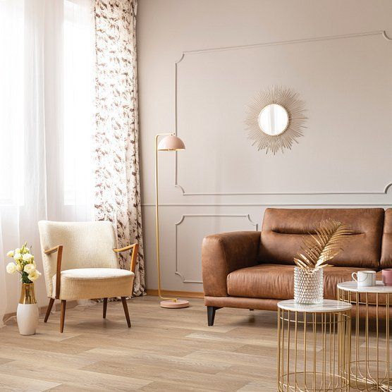 Living room with leather sofa, cream armchair, gold accents, and a sunny window.