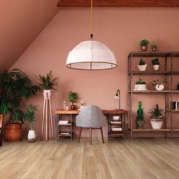 A bright room with wood floors and terracotta walls; a desk is surrounded by plants, and a hanging lamp.