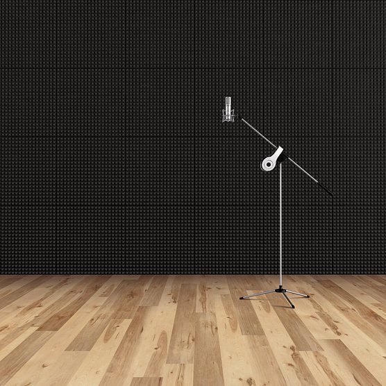 Microphone on stand in a soundproof recording studio with black acoustic panels and wood floor.