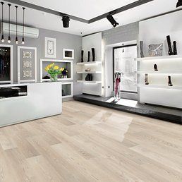 Light-wood-floored boutique with white shelves displaying shoes, a white counter, and a gray accent wall.