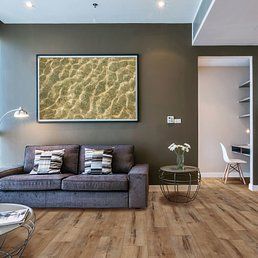 Living room with a gray sofa, framed water surface art, and light wood-look flooring.
