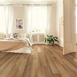 Bedroom with light wood floors, sheer white curtains, and a bed with tan bedding.