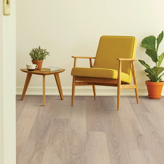 A room with light wooden floors, a yellow chair, a small table, and a potted plant.