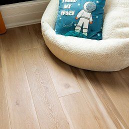 Light wood floor with a fluffy white dog bed and astronaut pillow.