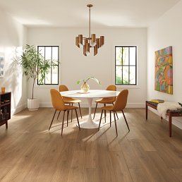 Dining room with wood floors, round table, orange chairs, windows, and abstract artwork.