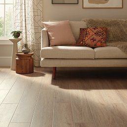Living room with light wood floors, beige sofa with pillows, and a small side table.