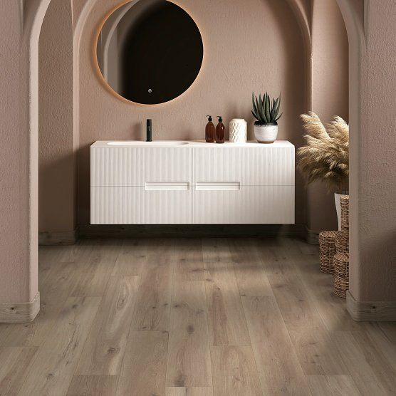 Bathroom with wood-look flooring, white floating vanity, round mirror, and decorative plants in a warm, neutral colors.