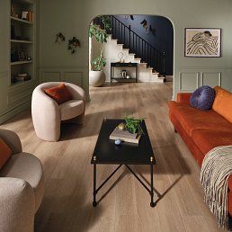 Living room with sage green walls, velvet sofa, and stairs in the background.