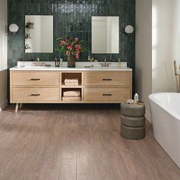 Bathroom with wood-look flooring, light wood vanity, dark green tiled wall, and a white tub.