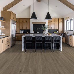 Kitchen with wood cabinets, island with black stools, and gray wood-look flooring.