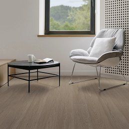A modern living room with a chair, table, and window; light wood floor.