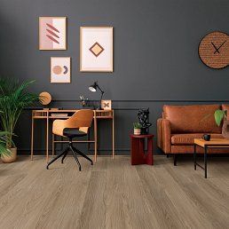 A cozy living room with wooden floors, a brown leather couch, and a desk with artwork on the wall.