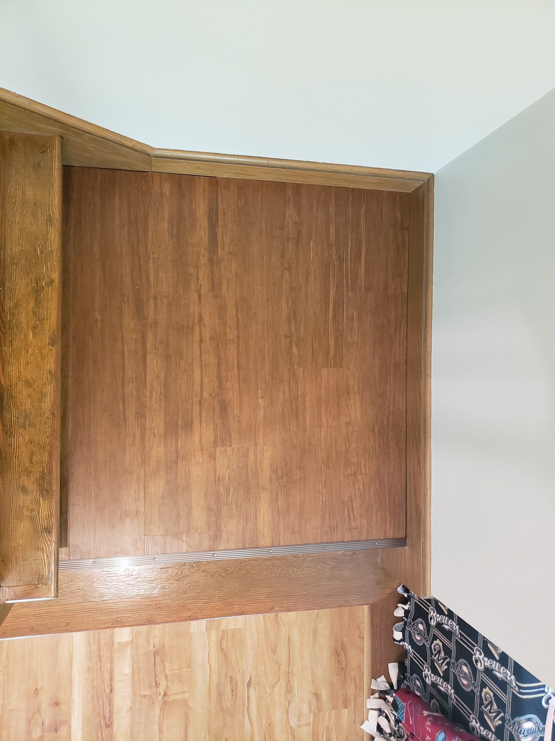 Wooden cabinets in a corner, with a white wall and a patterned cushion visible.