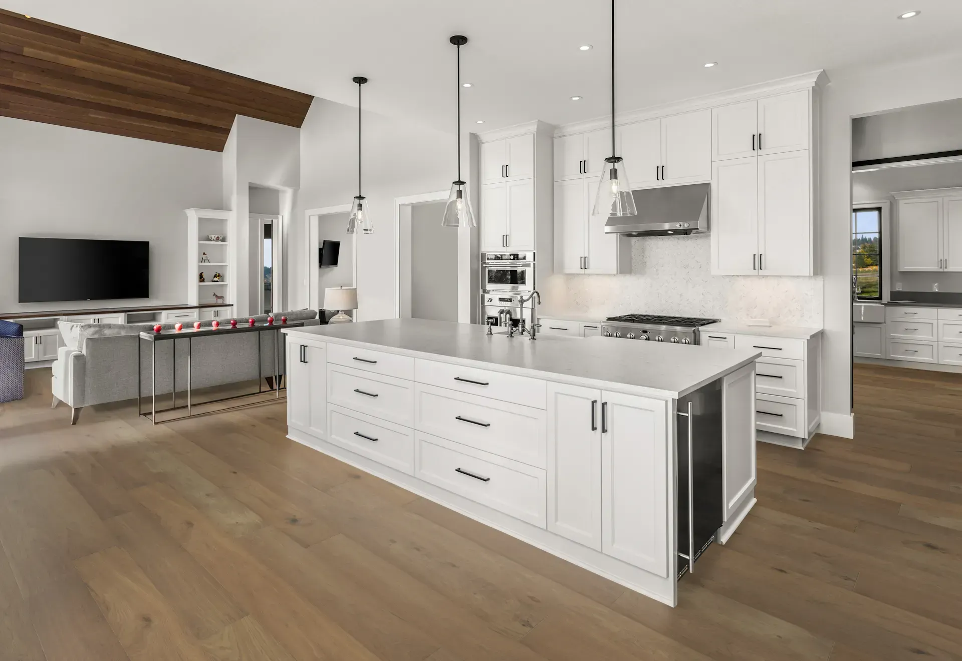 Spacious, white kitchen with large island, stainless steel appliances, and open concept to living area.