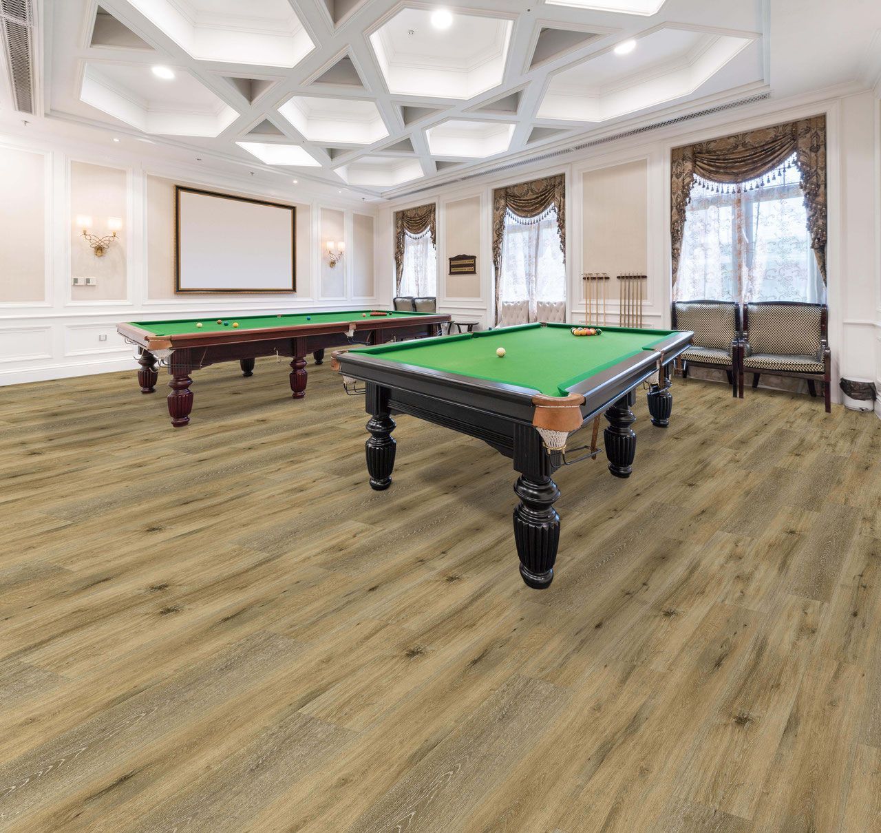A room with two pool tables. Oak flooring, ornate ceiling. Beige walls, window with curtains.