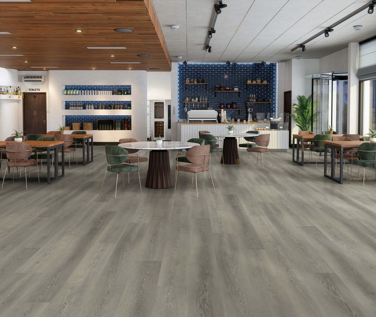 Spacious cafe with wooden floor, tables, and chairs; a bar with blue wall and bottles is in the back.