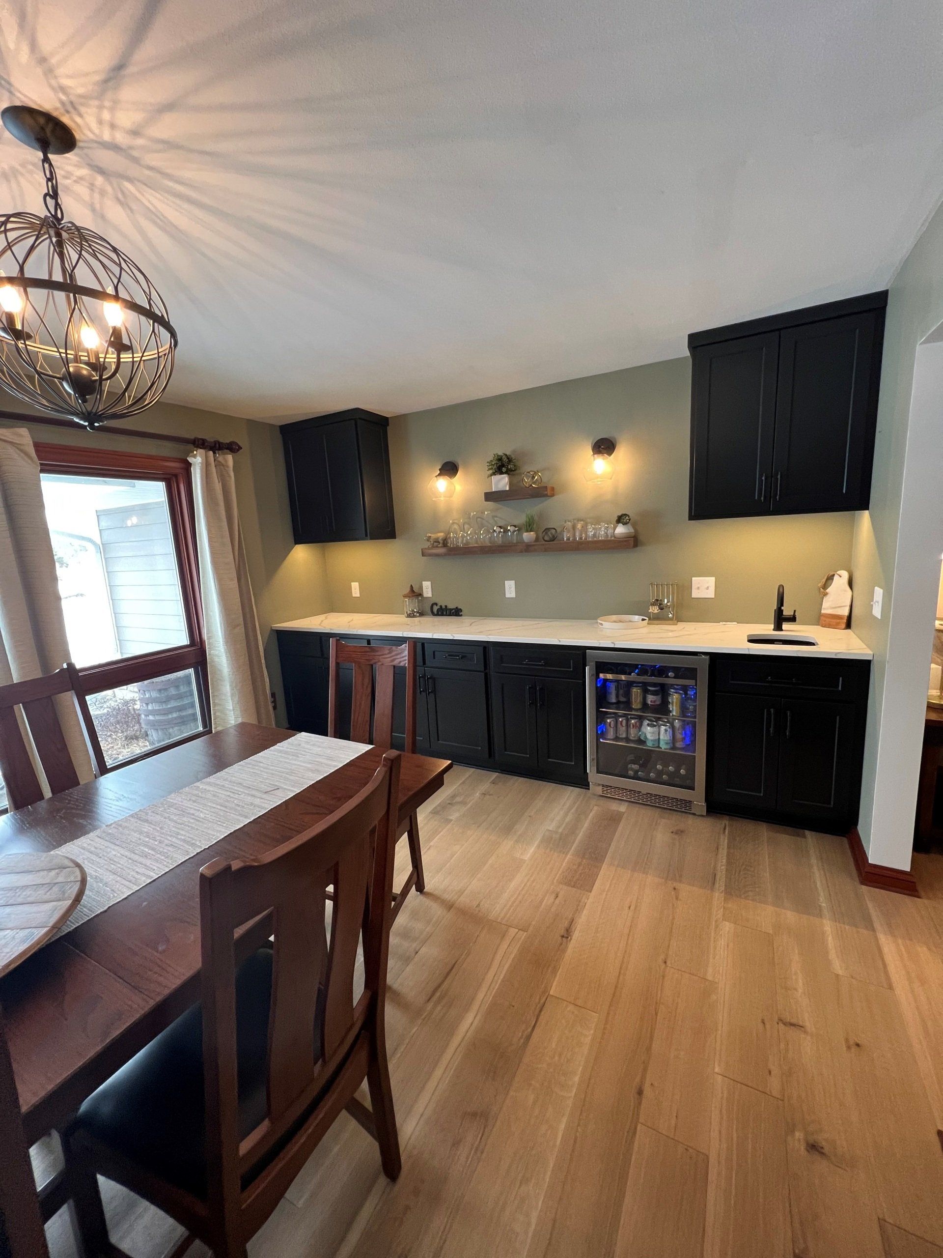 Dining room with a built-in black bar, white countertop, shelves with plants, and hardwood floor.