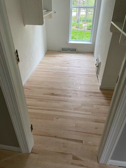 Light wood floor in a small room with a window, beige walls, and white trim.
