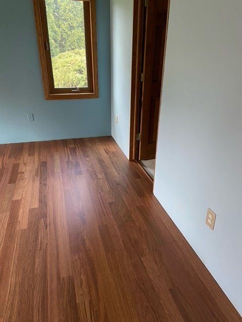 Room with wood floor, blue and white walls, and a window overlooking trees.