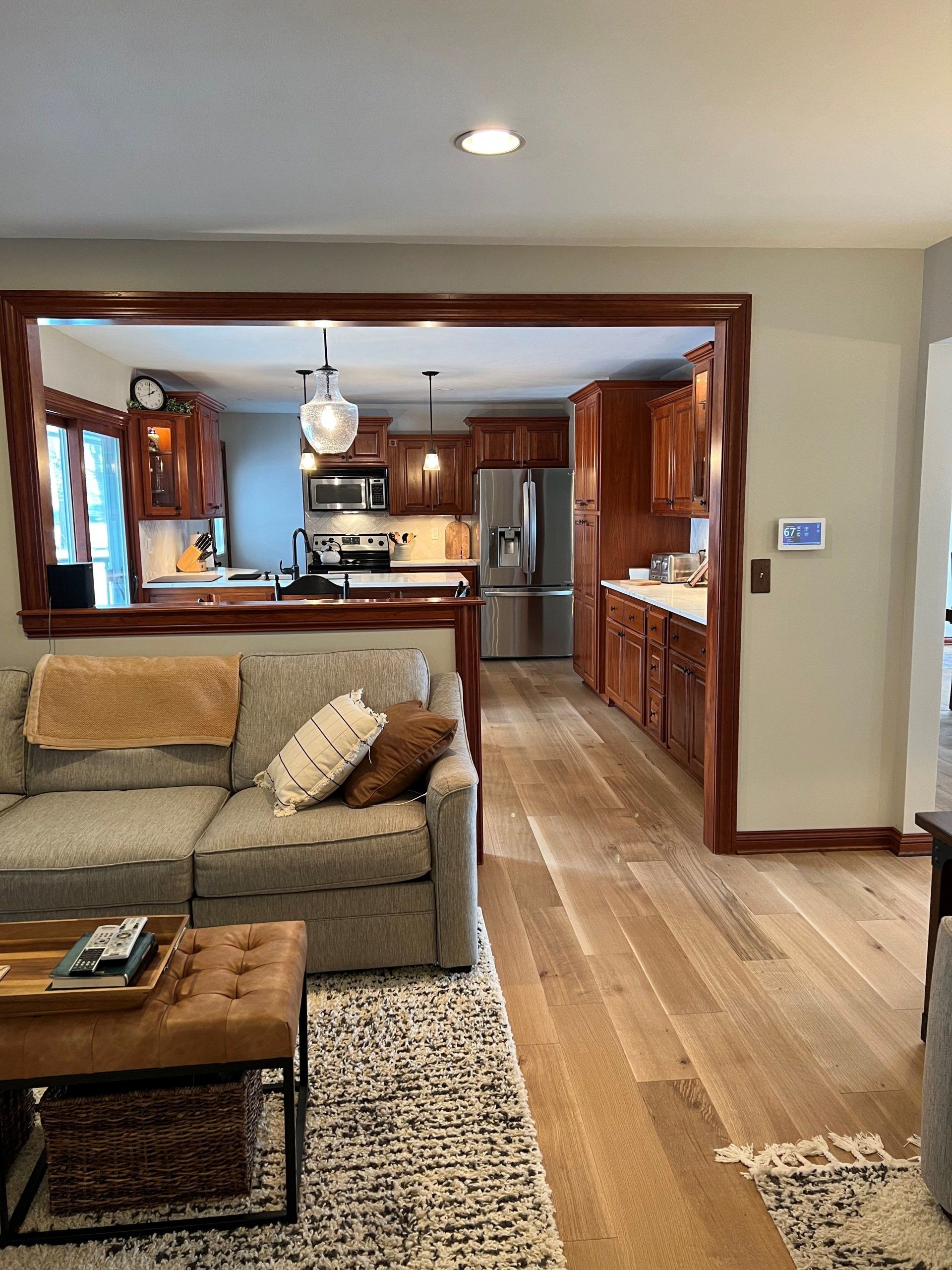 Living room with open kitchen. Gray couch, hardwood floor, cherry cabinets, and stainless steel appliances.
