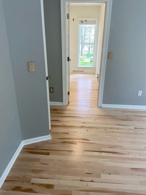 View down a hallway with light hardwood floors, gray walls, and doorways.
