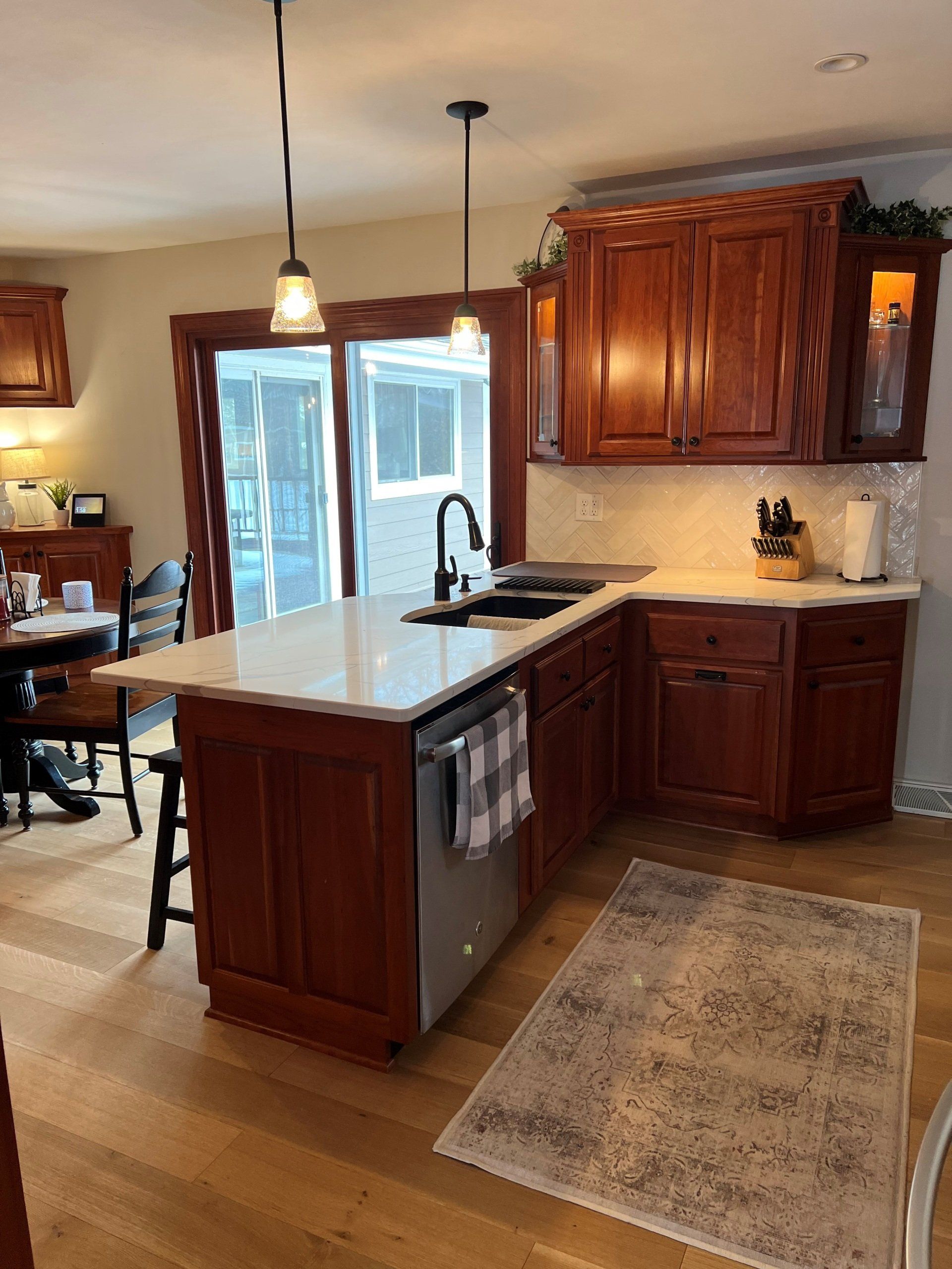 A kitchen with cherry cabinets, white countertops, and a stainless steel dishwasher.