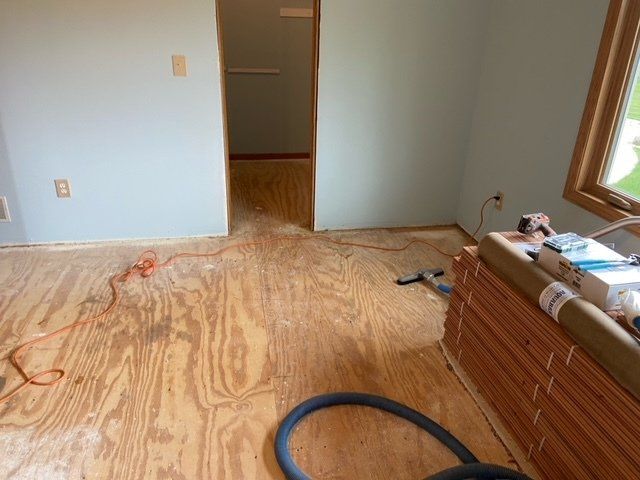 Room with exposed plywood floor, blue walls, door, and a stack of flooring materials.
