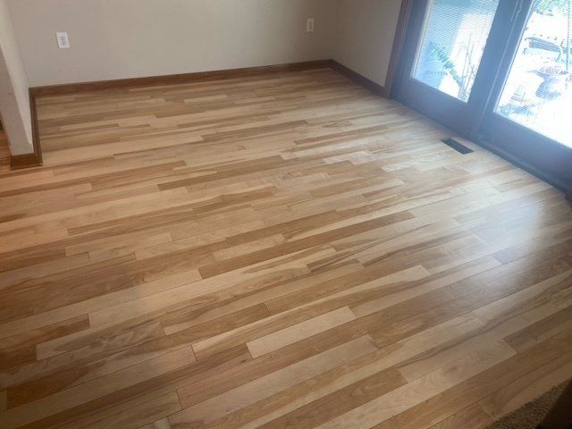 Light wooden flooring in a room, with a doorway and natural light coming in.