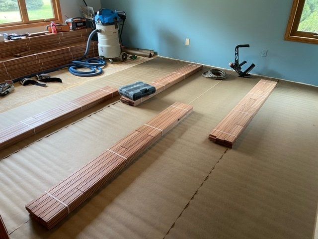 Bundles of reddish-brown hardwood flooring laid out on beige foam mats in a room with blue walls.