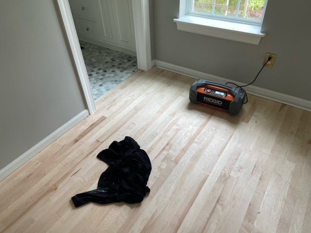 Light wood floor with black cloth, gray walls, bathroom door, and an orange radio plugged into a wall.