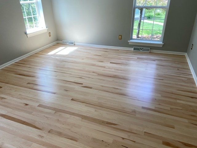 An empty room with hardwood floors and two windows