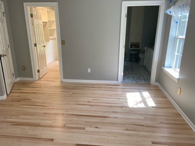 Bedroom with light-colored hardwood floors, gray walls, and a walk-in closet and bathroom in the background.