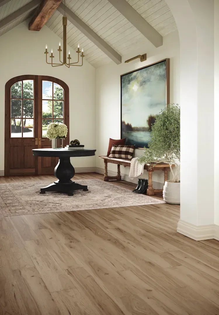 A warm, inviting entryway with hardwood floors, a round table, and large artwork.