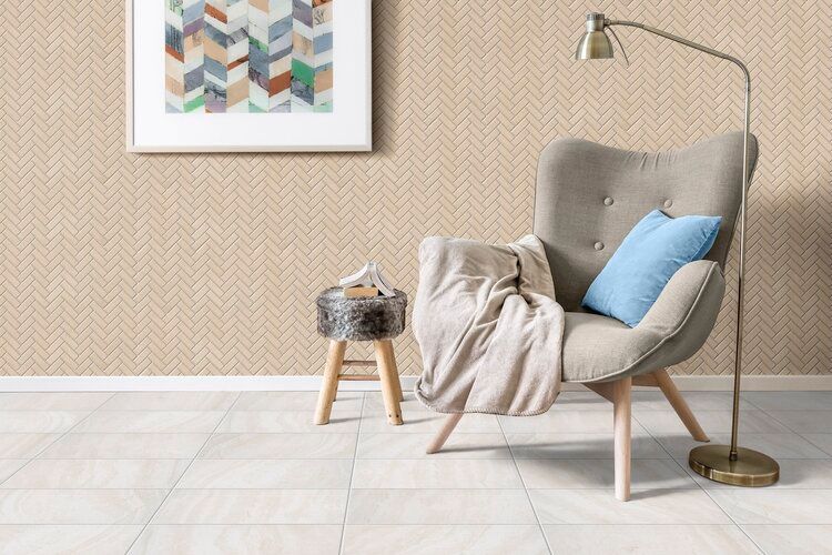 Cozy beige chair with a blanket and blue pillow, next to a lamp and stool, against a patterned wall.