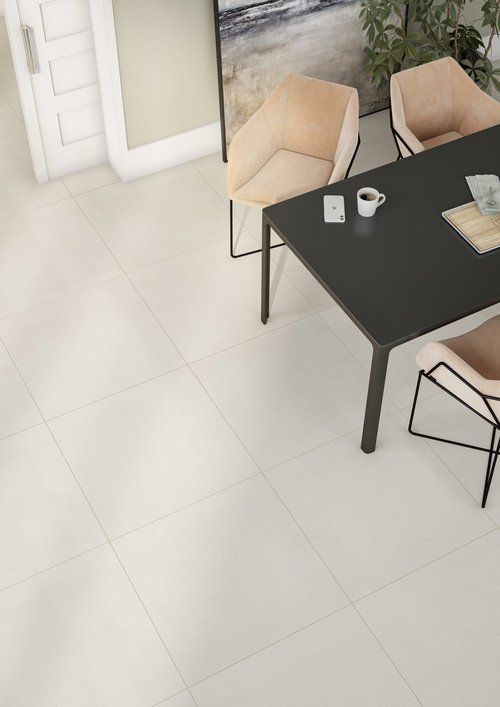 Overhead view of a dining room with a black table, four tan chairs, and white tiled floor.