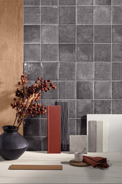 Dark gray square tiles form a backdrop for decorative items: vase, red block, fabric, and samples.