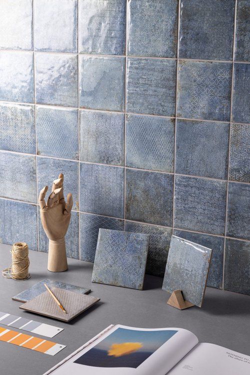 Blue square tiles on a wall with samples, art supplies, and a wooden hand; design concept.
