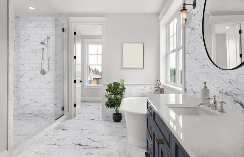 Spacious white bathroom with marble tile, walk-in shower, navy vanity, and large window.