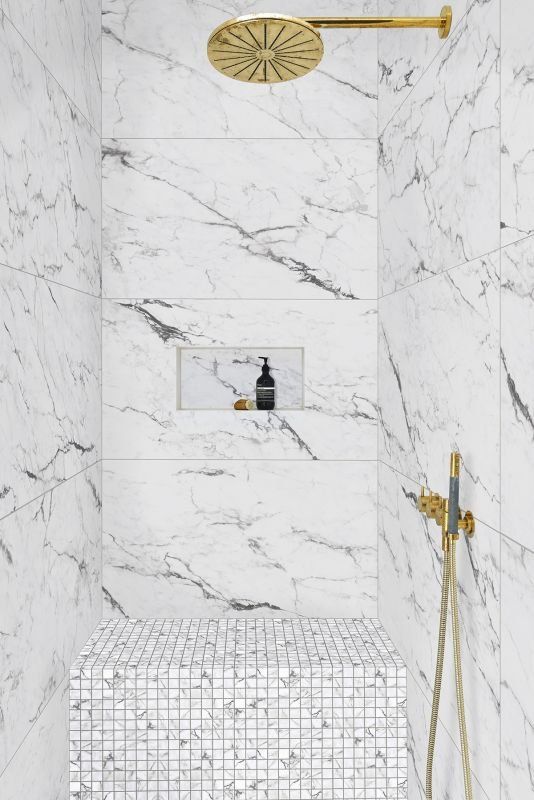 Marble-tiled shower with gold fixtures. Built-in bench and shelf. White and gray veined tile.