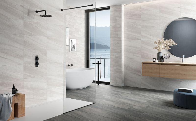 Modern bathroom with gray and white tile, wood accents, and large window overlooking water.