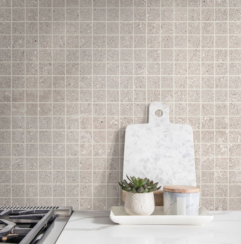 Beige square mosaic tile backsplash with marble cutting board and kitchen countertop with potted plant.