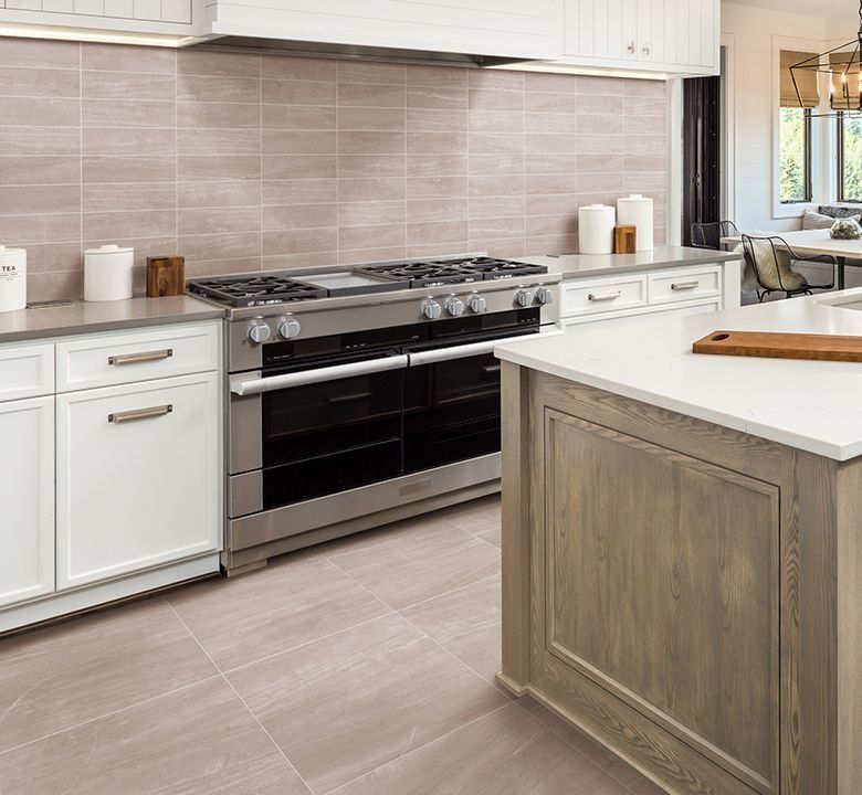 A modern kitchen with white cabinets, stainless steel appliances, and a light brown island.